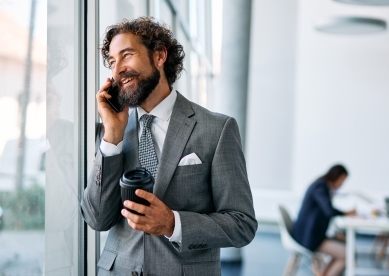 Smiling businessman talking on phone, holding coffee cup in office